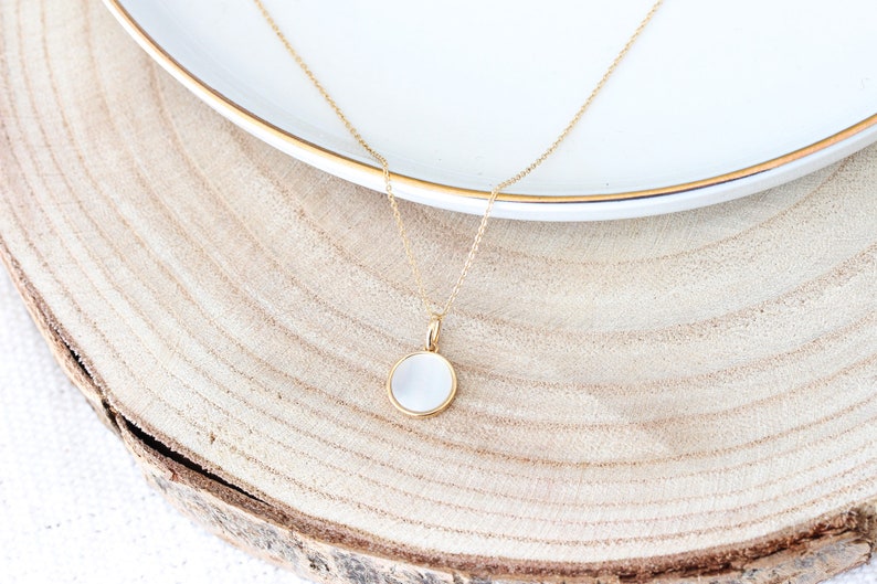 May include: A gold chain necklace with a white round pendant. The pendant is made of mother of pearl and has a gold rim.