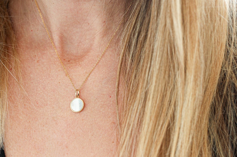 May include: A gold chain necklace with a round white pendant.
