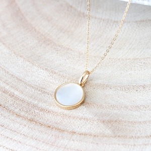 May include: A gold chain necklace with a round white pendant. The pendant has a gold rim.