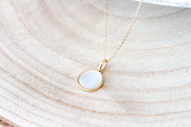May include: A gold chain necklace with a round white pendant. The pendant has a gold rim.