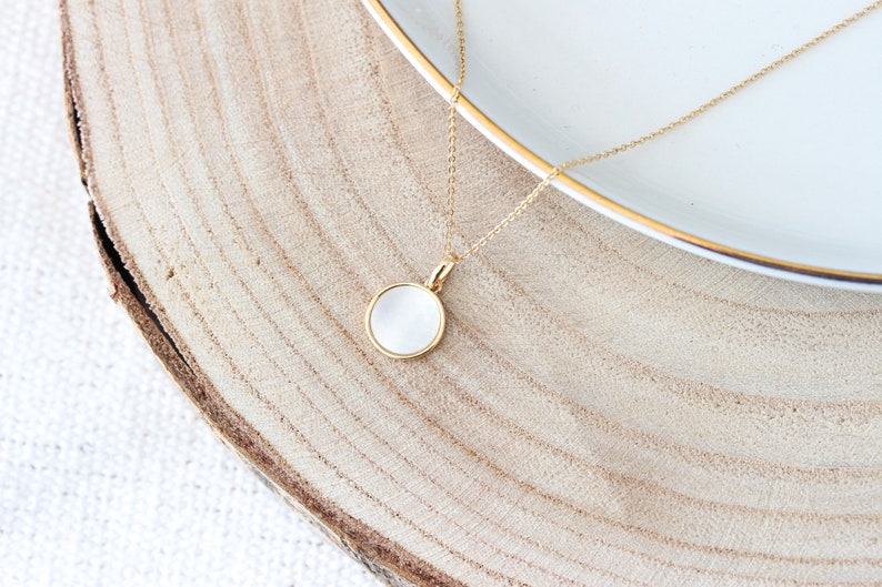 May include: A gold chain necklace with a white round pendant. The pendant is set in a gold frame and has a smooth, slightly textured surface.
