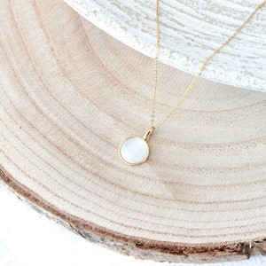 May include: A gold chain necklace with a white round pendant. The pendant is made of a smooth, white material and has a gold rim.