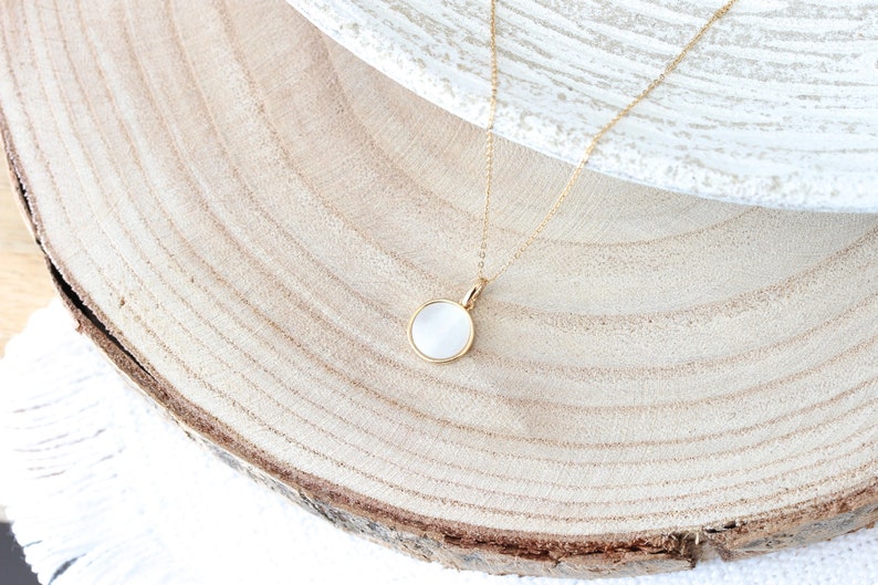 May include: A gold chain necklace with a white round pendant. The pendant is made of a smooth, white material and has a gold rim.