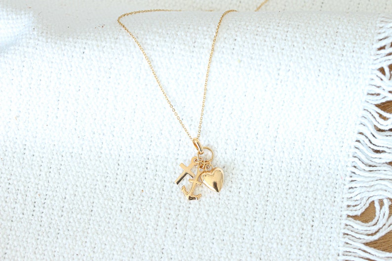 May include: A gold chain necklace with a charm featuring a heart, cross, and anchor.