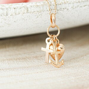 May include: Gold charm necklace with a heart, cross, and anchor pendant. The charms are attached to a gold chain.