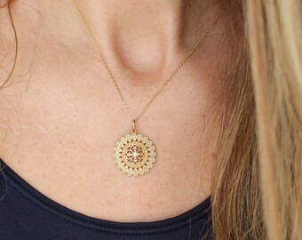May include: A gold necklace with a delicate, circular pendant featuring a floral design. The pendant is intricate and has a slightly raised center.