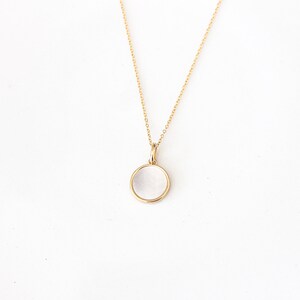 May include: A gold chain necklace with a round, white, opaque pendant.