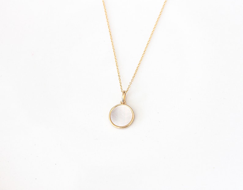 May include: A gold chain necklace with a round, white, opaque pendant.