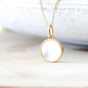 May include: A gold chain necklace with a round, white, mother-of-pearl pendant.