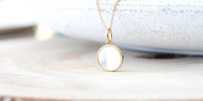 May include: A gold chain necklace with a round, white, mother-of-pearl pendant.