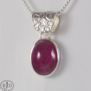 Può includere: Una collana con ciondolo in argento con una pietra ovale rosa e un design floreale dettagliato sulla ghiera.