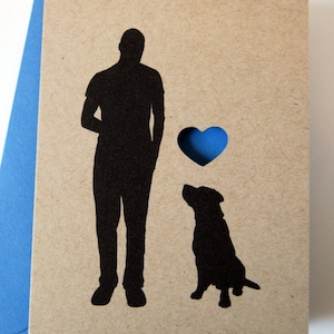 Puede incluir: Tarjeta de felicitaci&oacute;n con silueta negra de una persona y un perro, con un coraz&oacute;n recortado. La tarjeta es de color beige con un coraz&oacute;n azul y un sobre azul.