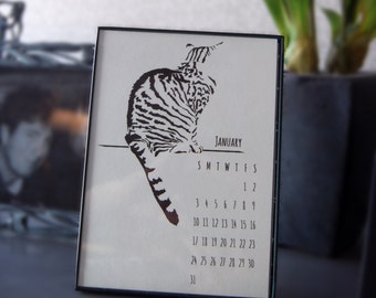 Könnte beinhalten: Eine schwarz-weiße Silhouette einer Katze auf weißem Hintergrund mit einem Januar-Kalender darunter. Der Kalender zeigt die Wochentage und die Zahlen von 1 bis 31.