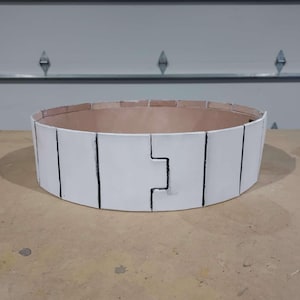 Könnte beinhalten: Ein weißes, segmentiertes, kreisförmiges Objekt mit schwarzen Linien und einem einzigartigen ineinandergreifenden Design. Der Innenraum ist hellbraun. Das Objekt liegt auf einer hellbraunen Oberfläche.