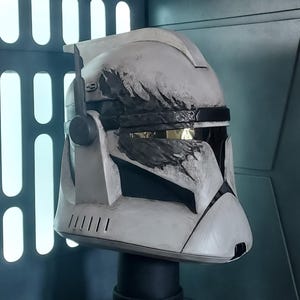 May include: A white clone trooper helmet featuring a prominent black claw mark graphic across the visor area. The helmet includes a side-mounted antenna, a dark horizontal visor, and weathered detailing throughout the white surface finish.