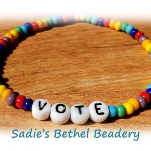 May include: Rainbow beaded bracelet with the word "VOTE" spelled out in white letter beads.