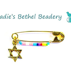 May include: Gold safety pin with a rainbow beaded charm and a gold Star of David pendant. Sadie's Bethel Beadery.
