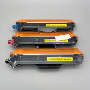 May include: Three new printer toner cartridges. The cartridges are black with orange protective covers. Each cartridge has a different color accent: blue, pink, and green. Each cartridge is labeled with the letter C, M, or K.