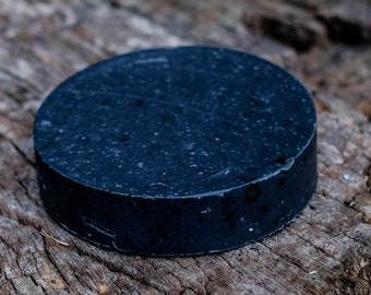 Puede incluir: Una pastilla de jabón redonda de color azul oscuro sobre una superficie de madera.