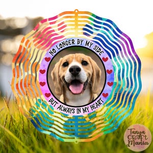 May include: A circular wind spinner with a photo of a beagle dog, surrounded by the text "NO LONGER BY MY SIDE BUT ALWAYS IN MY HEART." The design incorporates rainbow colours and red heart motifs, ideal for pet owners.