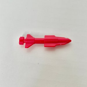 May include: A bright pink plastic toy missile with a pointed nose and a small fin on the tail.
