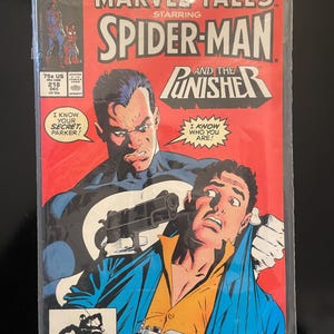 May include: A comic book cover featuring Spider-Man and the Punisher. The Punisher is holding a gun to Spider-Man's head. The cover is red with the title "Marvel Tales Starring Spider-Man and the Punisher" in white letters. The comic book is issue number 218.