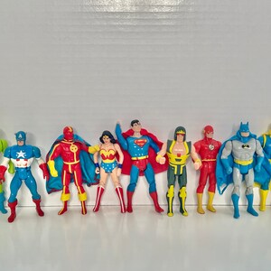 May include: A collection of eight superhero action figures, including Superman, Batman, Wonder Woman, The Flash, Captain America, Green Lantern, and two others. The figures are all in various poses and are made of plastic.