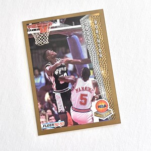 May include: A basketball trading card featuring David Robinson of the San Antonio Spurs and Manning. The card has a gold border and the NBA logo. The card is from the Fleer 92-93 series.