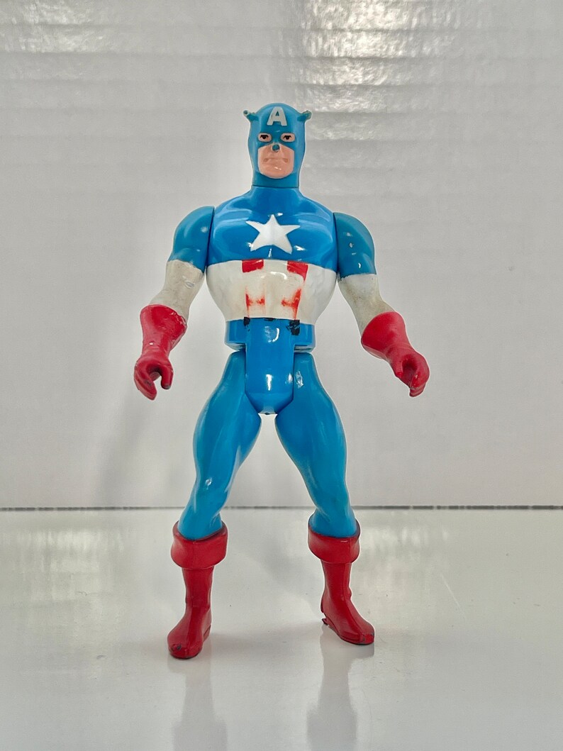 May include: A vintage action figure of Captain America, wearing his iconic red, white, and blue costume. The figure has a classic design and is in good condition.