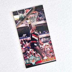 May include: A basketball trading card featuring Clyde Drexler of the Portland Trail Blazers in action. The card shows Drexler dunking a basketball, with the words "NBA JAM SESSION" and "'93-'94" visible. The card has a white border.