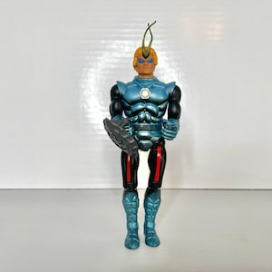 May include: A blue and silver action figure with a green antenna on its head. The figure is holding a black shield in its left hand. The figure has a white star on its chest.