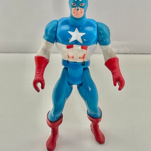 May include: A vintage action figure of Captain America, wearing his iconic red, white, and blue costume. The figure has a blue body, red gloves, and red boots. The figure has a white star on its chest and the letter 'A' on its forehead.
