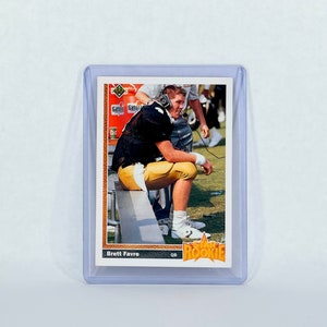 May include: A vintage trading card featuring Brett Favre, a quarterback, wearing a black and gold uniform. The card is from the Star Rookie series and has a green and gold border.