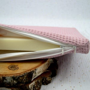 Zoom sur la fermeture éclair ouverte d'un petit matelas en mousse imperméable pour lapin et autres petits animaux pour visualiser sa composition: un matelas en mousse recouvert d'une housse imperméable puis d'une deuxième housse absorbante en tissu éponge nid d'abeille
