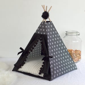 Peut inclure: Un tipi pour animaux de compagnie &agrave; motifs noirs et blancs avec un coussin blanc &agrave; l'int&eacute;rieur. Le tipi pr&eacute;sente un motif g&eacute;om&eacute;trique et est orn&eacute; de pompons noirs. Le sommet est orn&eacute; de b&acirc;tons en bois et d'un pompon noir.