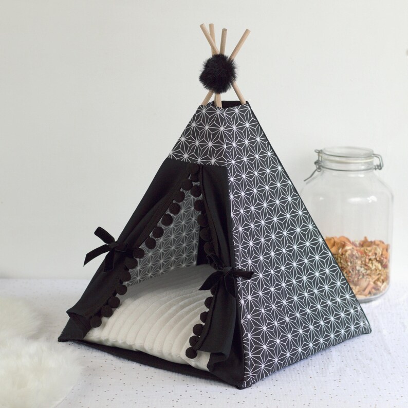 Peut inclure: Un tipi pour animaux de compagnie &agrave; motifs noirs et blancs avec un coussin blanc &agrave; l'int&eacute;rieur. Le tipi pr&eacute;sente un motif g&eacute;om&eacute;trique et est orn&eacute; de pompons noirs. Le sommet est orn&eacute; de b&acirc;tons en bois et d'un pompon noir.