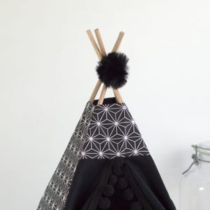 Gros plan sur le haut d'un tipi pour lapin de compagnie noir et à motif asanoha décoré avec un ruban à gros pompons noir et un gros pompons en fausse fourrure noir
