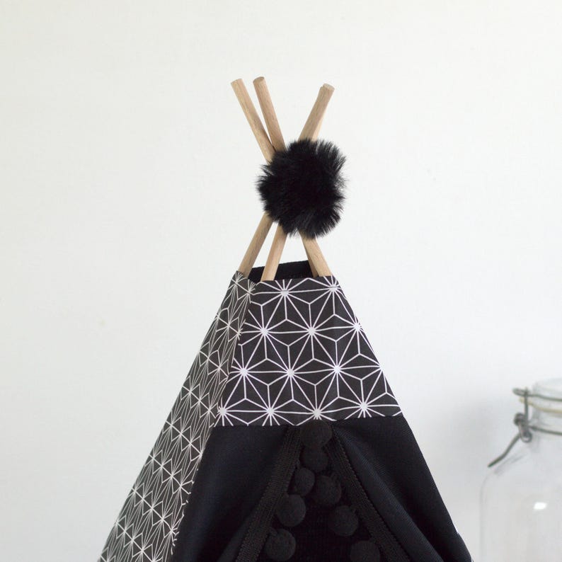 Gros plan sur le haut d'un tipi pour lapin de compagnie noir et à motif asanoha décoré avec un ruban à gros pompons noir et un gros pompons en fausse fourrure noir