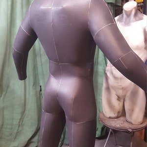 May include: A gray, full-body, fabric mannequin with marked lines for sewing. The mannequin is standing on a wooden platform.