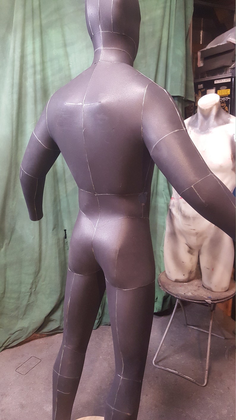 May include: A gray, full-body, fabric mannequin with marked lines for sewing. The mannequin is standing on a wooden platform.