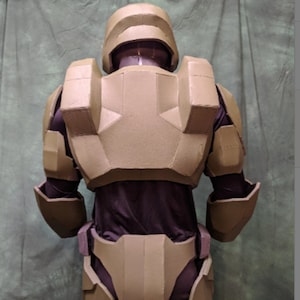 May include: A tan-colored, foam-padded, full-body armor costume. The armor is designed to resemble a futuristic soldier's suit. The armor is made of multiple pieces that are connected together. The armor is worn by a person, but the person is not visible in the image.