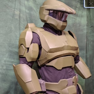 May include: A green and brown plastic costume of a futuristic soldier. The costume includes a helmet, chest plate, shoulder pads, and arm guards.