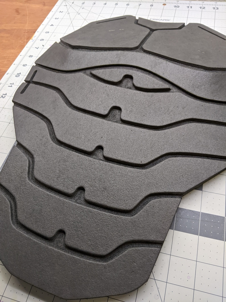 Puede incluir: Una pieza de armadura de espuma negra con una superficie texturizada y una serie de l&iacute;neas curvas elevadas. La pieza de armadura tiene forma de torso y tiene una parte superior redondeada.