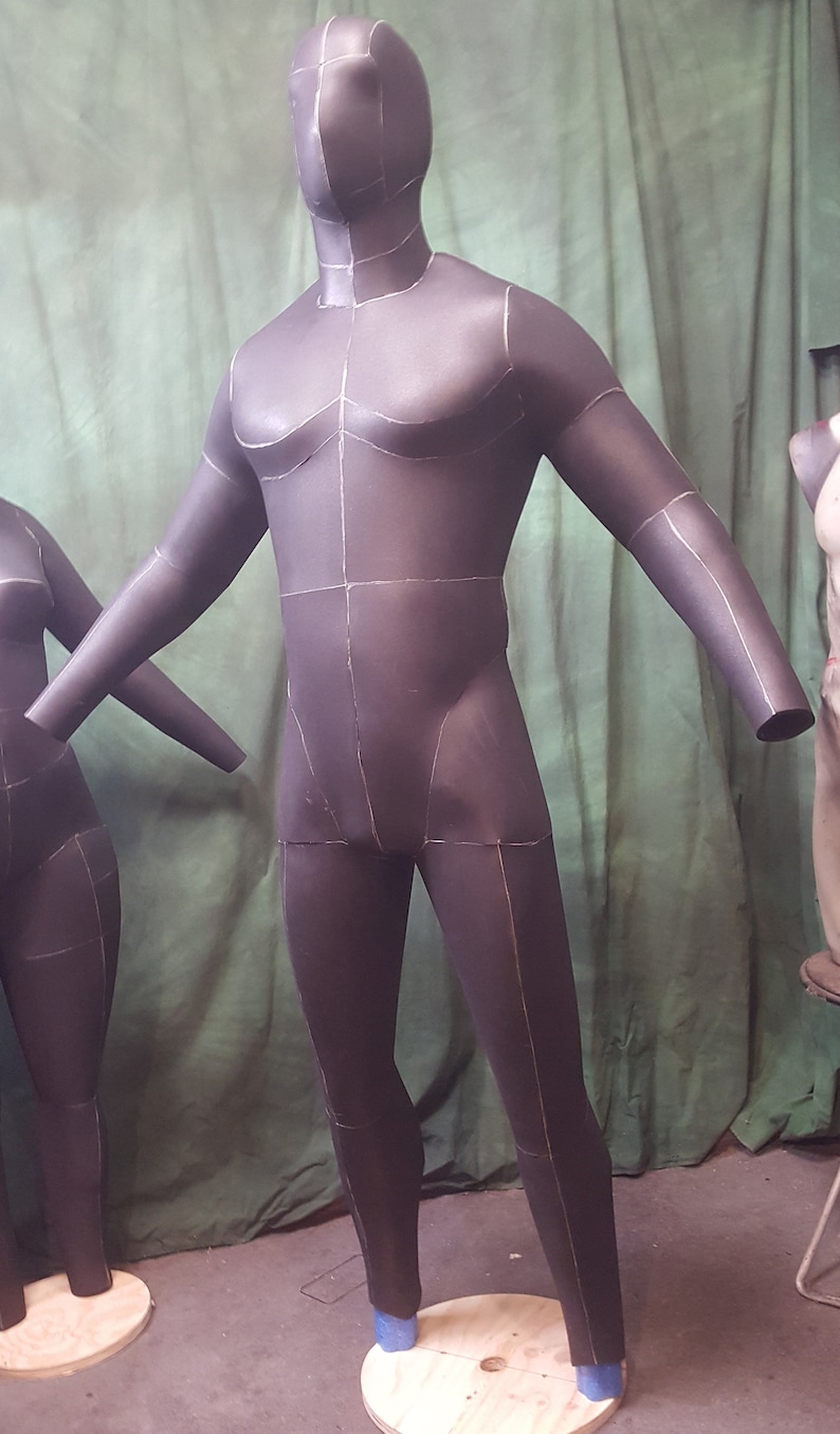 May include: A black, full-body mannequin with white lines drawn on it. The mannequin is standing on a wooden platform.