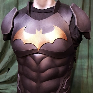Op de afbeelding: Een zwart en gouden Batman-kostuum borststuk met een gesculpteerd spierontwerp en een verhoogd vleermuissymbool.