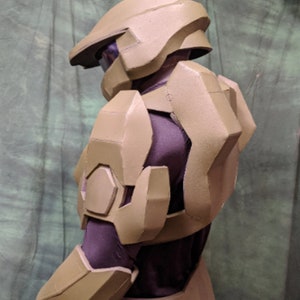 May include: A green and brown plastic costume helmet and armor for a video game character. The helmet has a visor and the armor has a detailed design.
