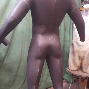 May include: A black foam mannequin with white lines drawn on it, showing the seams of a garment. The mannequin is standing on a wooden platform.