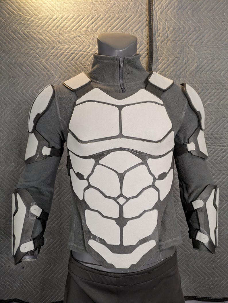 May include: A gray long-sleeved shirt with a white, segmented, armor-like chest piece and matching shoulder and forearm pieces.