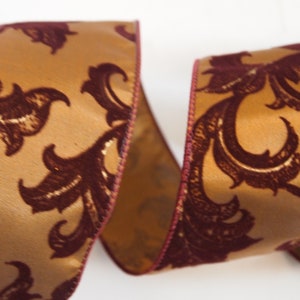 May include: Gold ribbon with a burgundy velvet floral pattern. The ribbon has a burgundy edge.