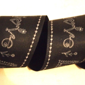 May include: Black ribbon with white decorative text and accents. The word "Love" is written in a decorative font, with hearts, flowers, and other embellishments. The edges are lined with small white hearts.